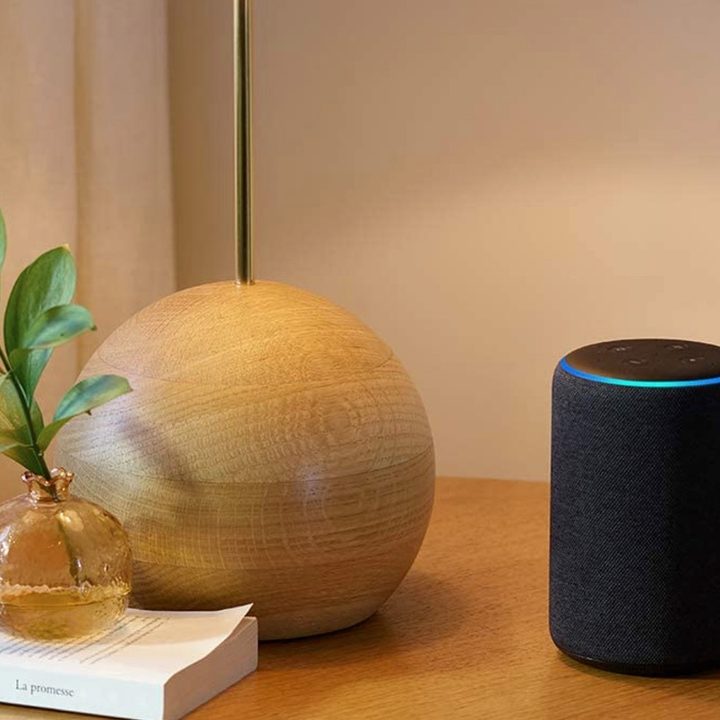 Amazon Echo on a table by a lamp and book.