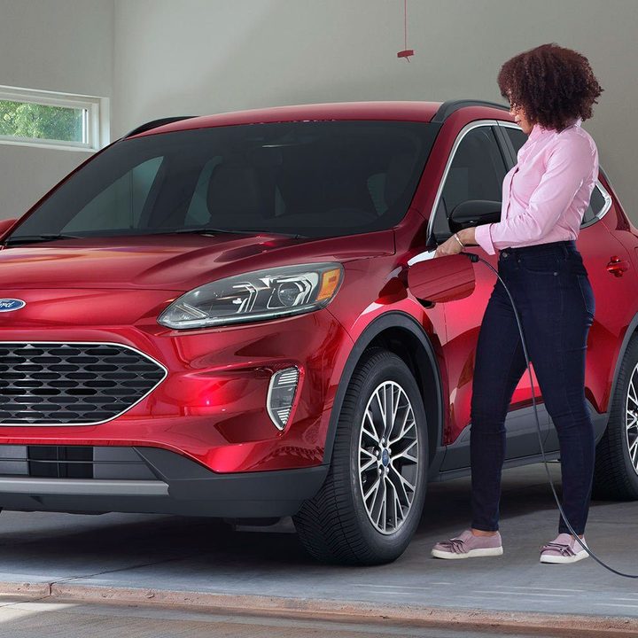 A woman plugs in a red Ford Escape PHEV in a garage.