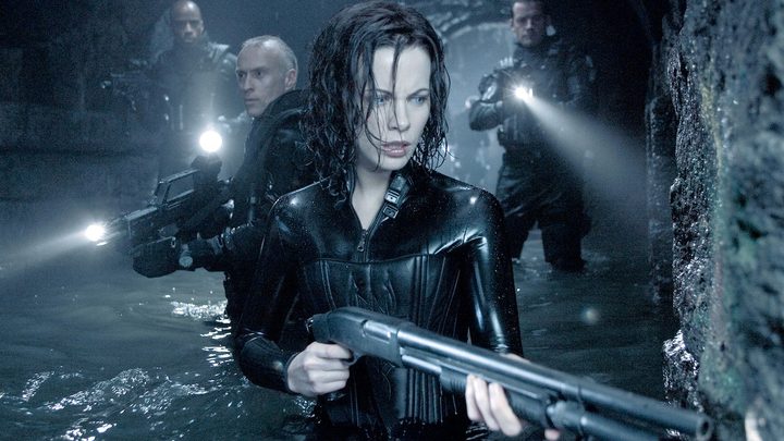 Kate Beckinsale as Selene holding a gun followed by two men in Underworld