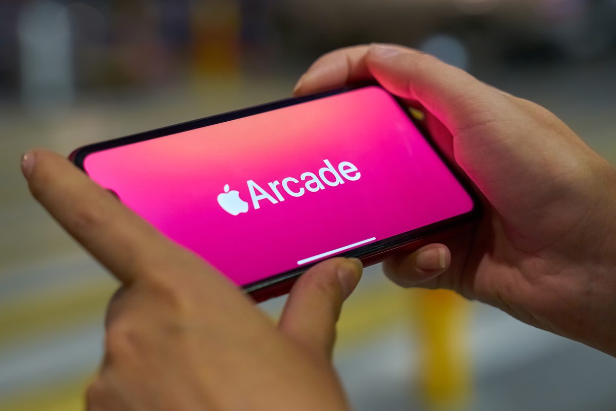 Woman holds the new iphone in landscape mode and subscribes to apple arcade with pink background