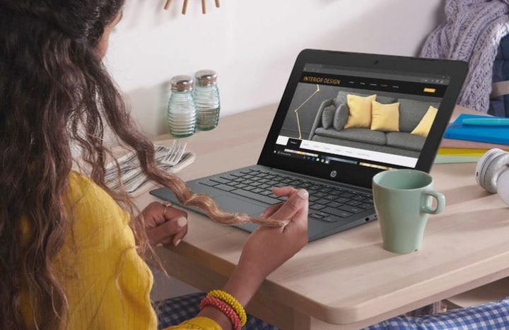 A woman in a yellow jumper sits at a desk with an HP Chromebook 11.6 open in front of her, and a mug alongside.