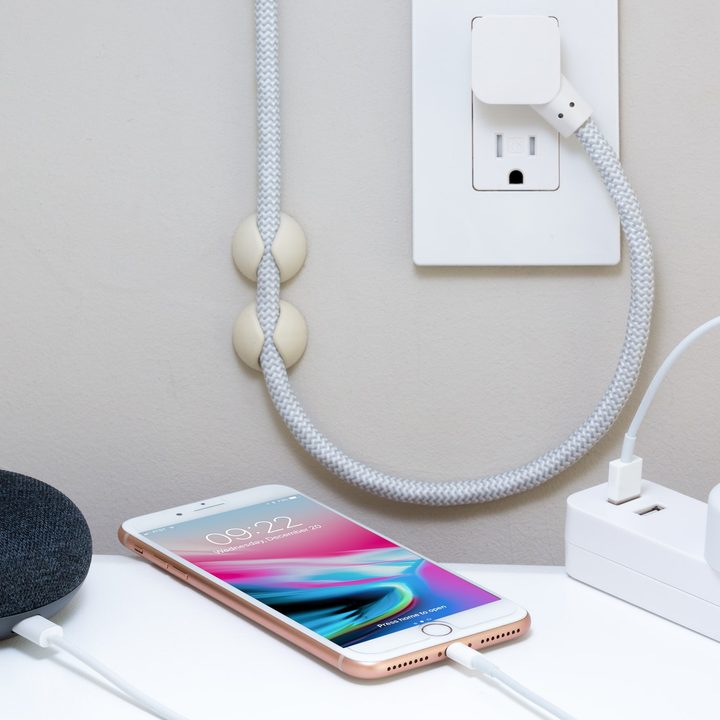 An iphone charging next to a smart home device and a power strip.