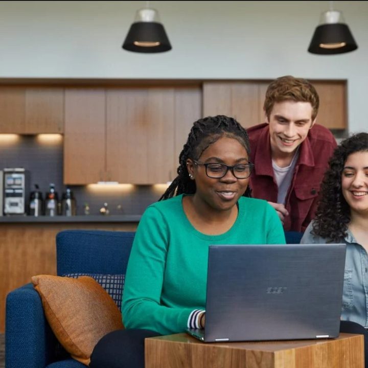 Three people sitting around a computer on a Teams call.