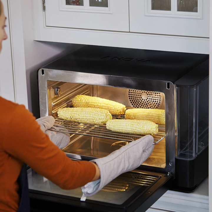 A woman cooking corn in a smart oven.