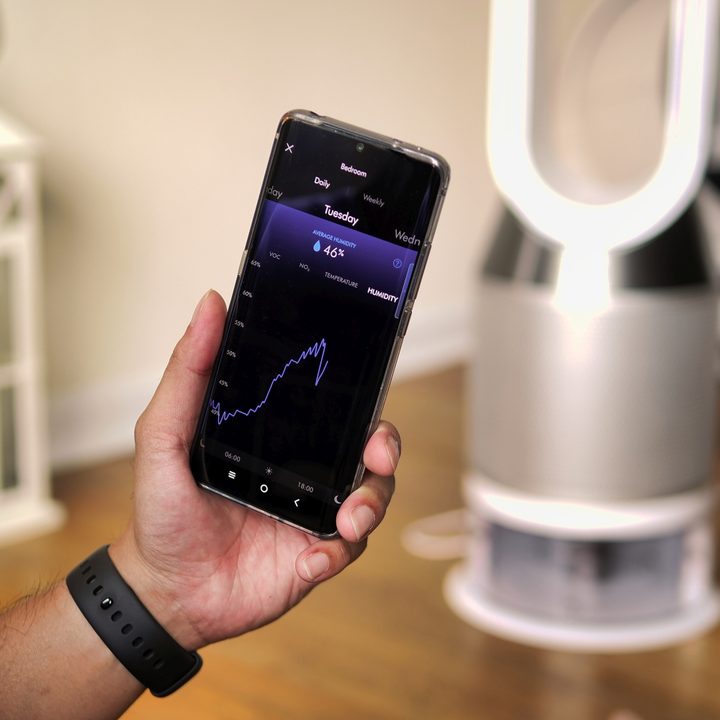 A person holds a phone displaying air quality data in front of the Dyson Pure Humidify Cool.