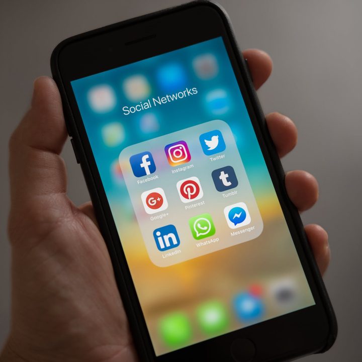 A hand holds an iPhone with social media apps open.
