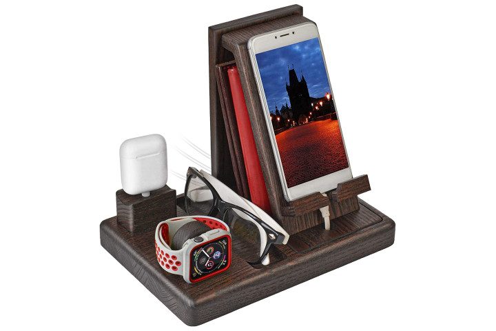 Photo shows an Apple iPhone, Apple Watch, and a pair of glasses in a solid wood docking station