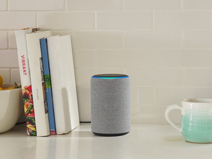 An Amazon Echo on a table in between a few books and a coffee mug.