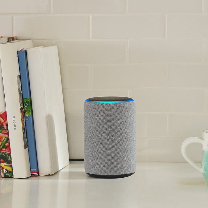 An Amazon Echo on a table in between a few books and a coffee mug.