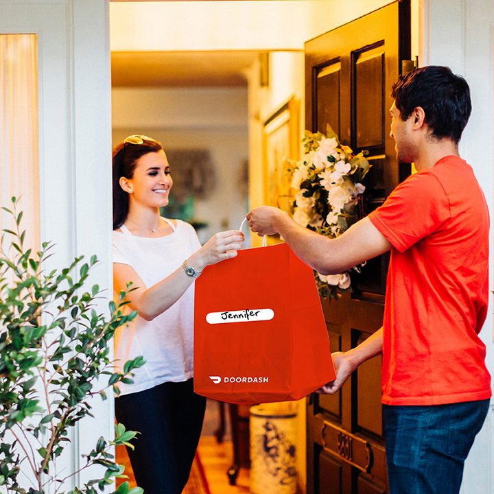 Woman accepting a Door Dash delivery from a man.