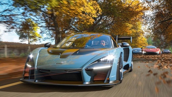 A blue car in Forza Horizon 4. It's on a road in front of some fall trees.