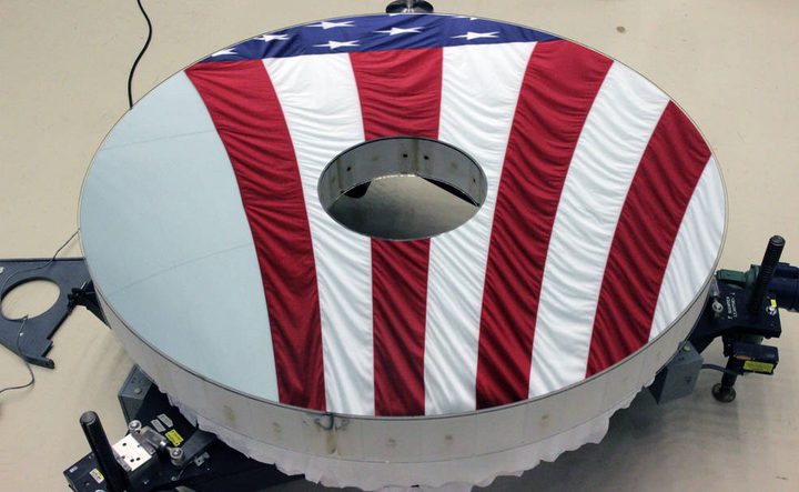 The Roman Space Telescope’s primary mirror reflects an American flag. Its surface is figured to a level hundreds of times finer than a typical household mirror.