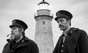 Willem Dafoe and Robert Pattinson in character with a lighthouse in the background in The Lighthouse.