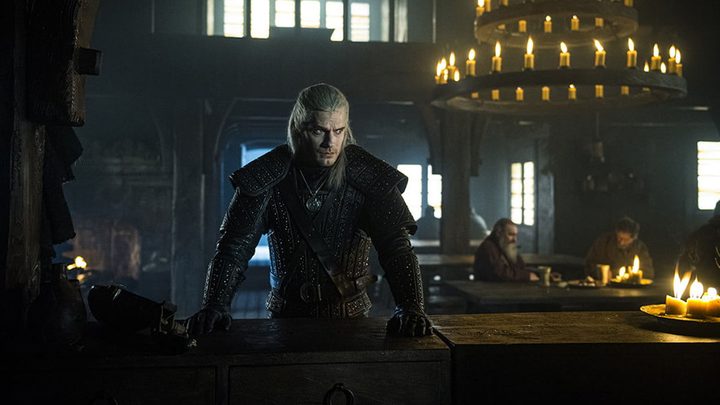 Geralt with his hands on a table looking serious in The Witcher.