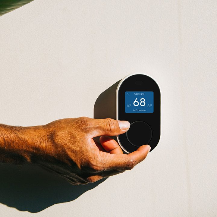 Wyze Smart thermostat installed on wall being adjusted.