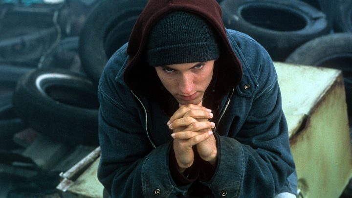 A man puts his hands together below his chin and sits.