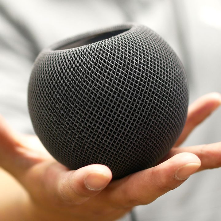HomePod Mini in a hand on its side.