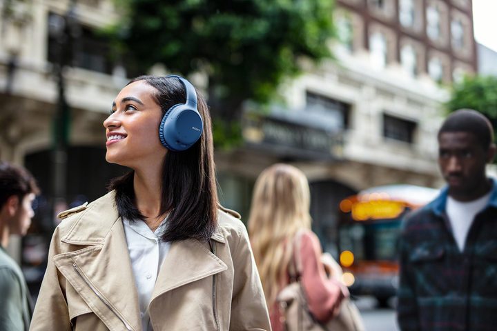 A woman wearing the Sony WH-CH710N smiling while outside and wandering around.