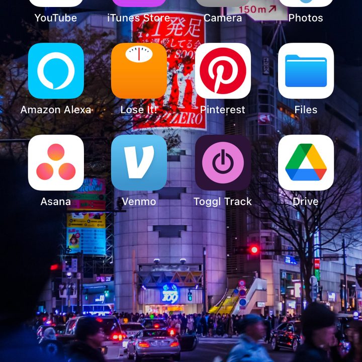 iPhone home screen with app icons on wallpaper of a busy city at night.