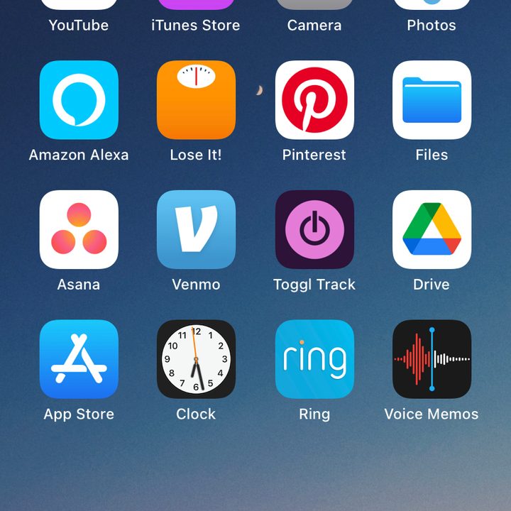 iPhone home screen with app icons on wallpaper of the sky at dusk.