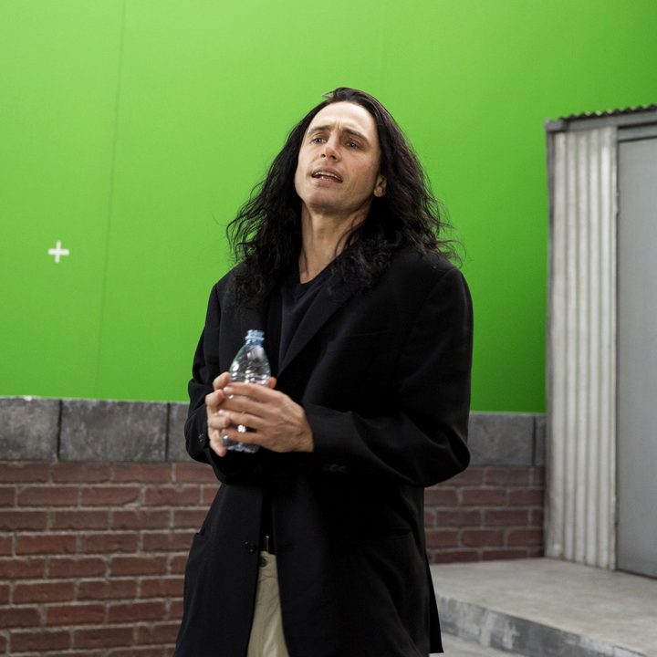 A man holds a water bottle and stands in front of a green screen.