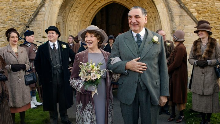 A man and woman walk hand-in-hand as a crowd looks on in Downton Abbey.