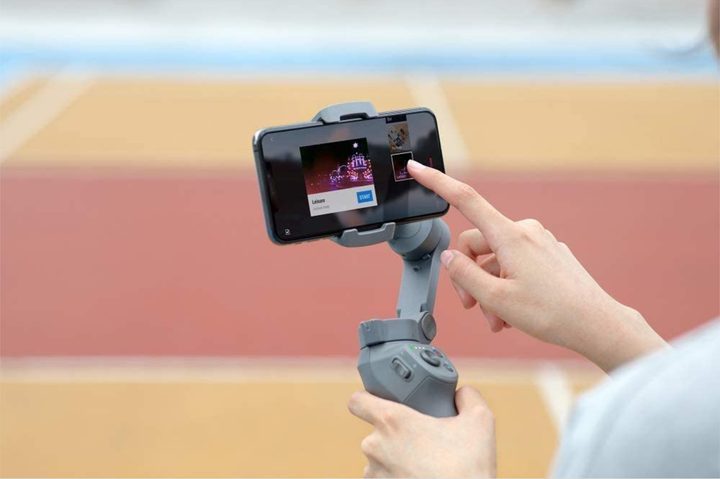 Person holding a DJI Osmo Mobile 3 gimbal while navigating on attached smartphone screen