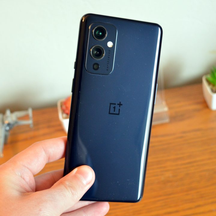 OnePlus 9 in black color against a table and fake plant