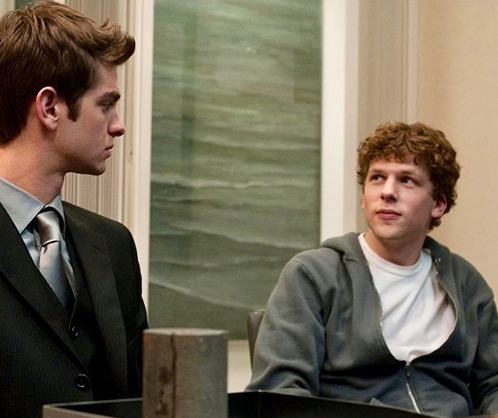 Andrew Garfield sits next to Jesse Eisenberg in The Social Network.