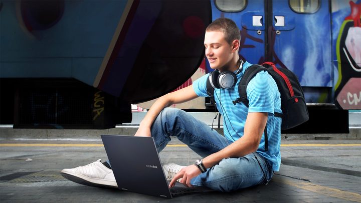 A college student sits on the ground using the Asus VivoBook Flip 14.