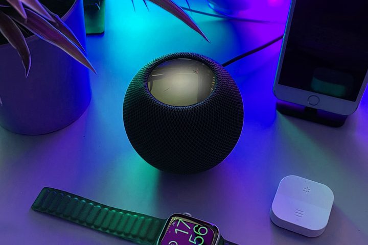 The Apple HomePod Mini on a table near an Apple Watch and an iPhone.