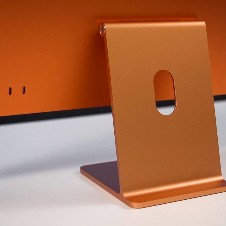 An orange 24-inch iMac seen from behind, with a focus on its hinge and ports.