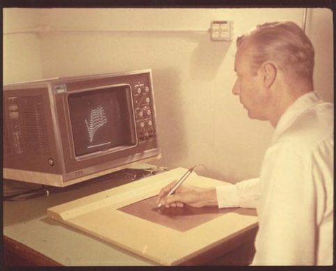Tom Ellis, one of the RAND tablet computer inventors. He has pen in his right hand writing on the tablet. On the screen are a series of graphic lines.