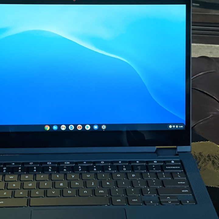 A Lenovo Yoga Chromebook sitting on t he desk in front of a shelf.