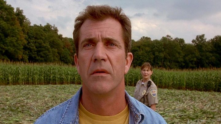 Rev. Graham looking to the distance with a female police officer standing behind him in the movie Signs.