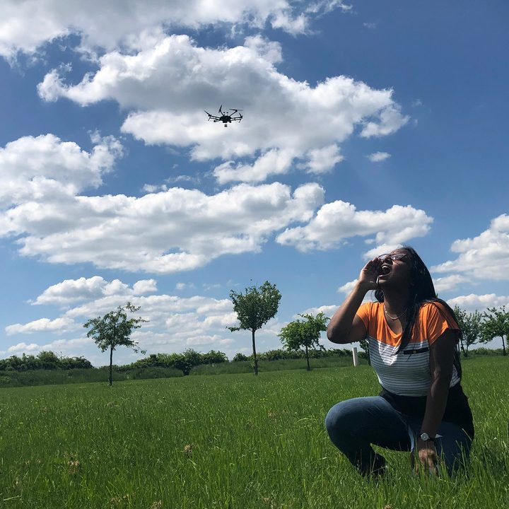 A woman in a field yells as a drone hovers overhead.