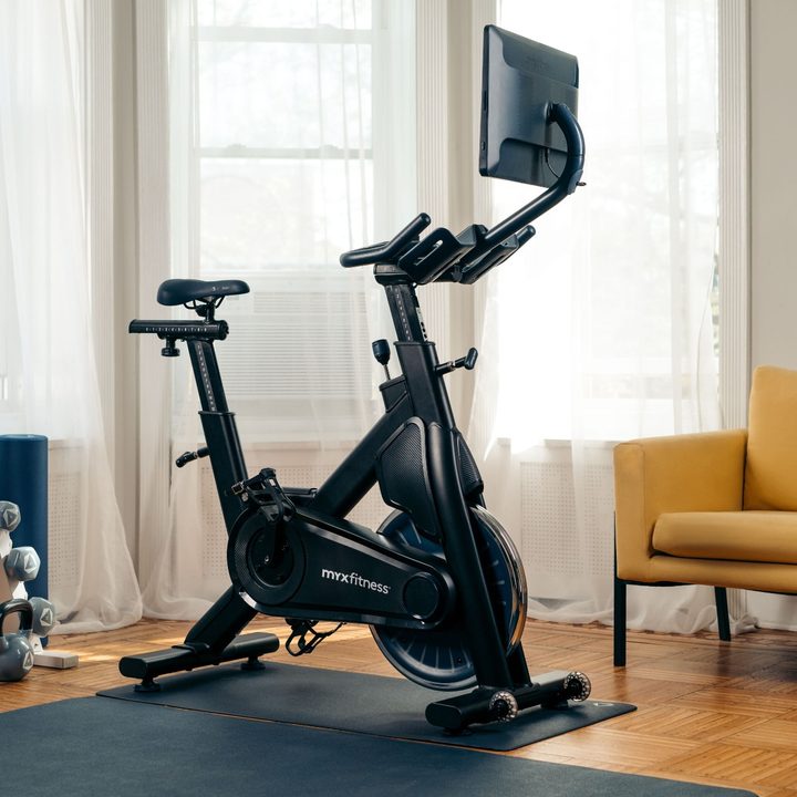 MYX II bike indoors with exercise mat and dumbbells.