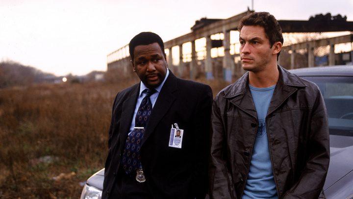 Two characters from The Wire leaning against a car.