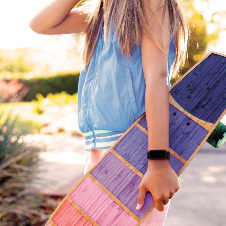 A girl holding onto skateboard while wearing Fitbit Ace 3.