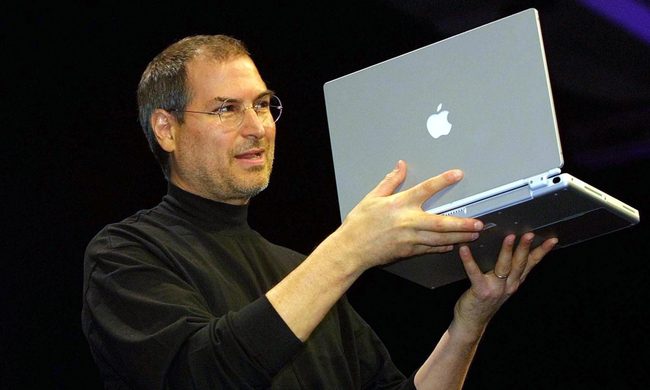 Former Apple CEO Steve Jobs holding a MacBook.