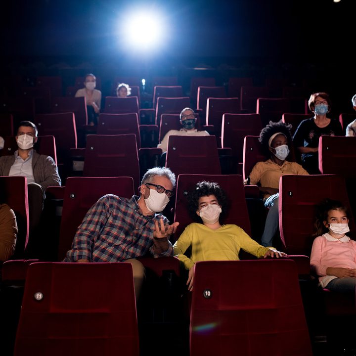 Kids and their grandparents wearing protective face masks while watching movies at the cinema.