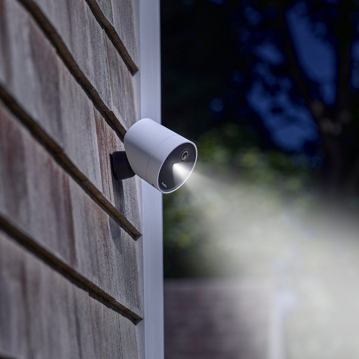 SimpliSafe Wireless Outdoor Security Camera mounted outdoors with spotlight on.