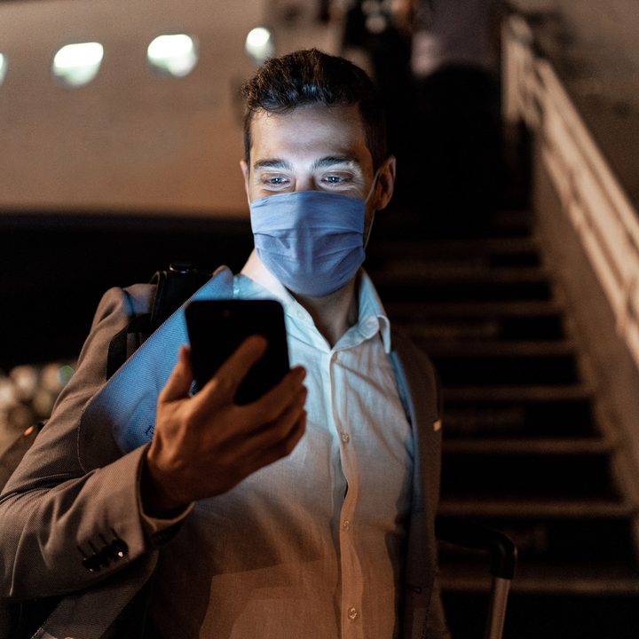 Businessman using mobile phone at airport using protective mask.