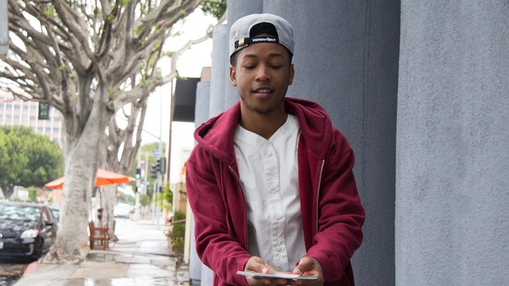 Jacob Latimore walks down the street holding cards.