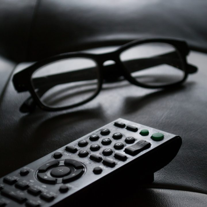 A black-and-white photo of a remote control and glasses.