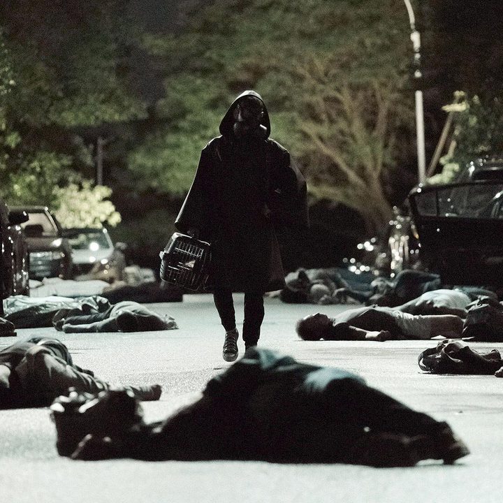 A masked character walks down a dark street.