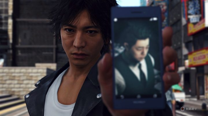 The main character of Judgment shows a picture on his phone to someone.