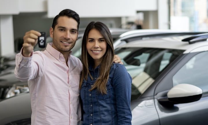 Happy couple buying a car at the dealership and holding the keys