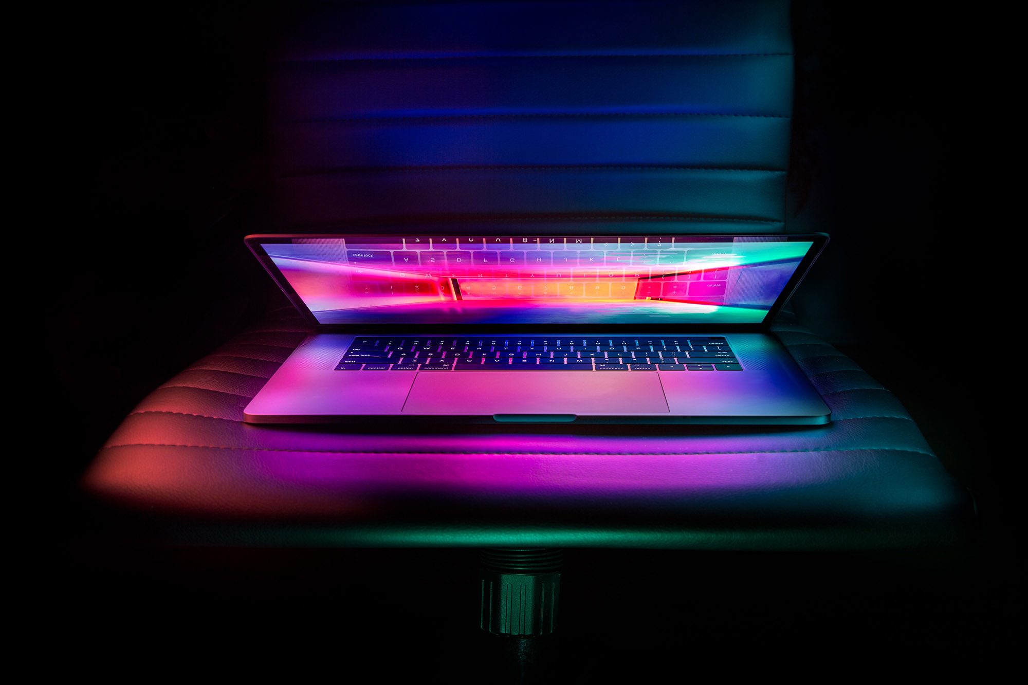 A Macbook Pro sitting on a chair, illuminated with neon lighting.
