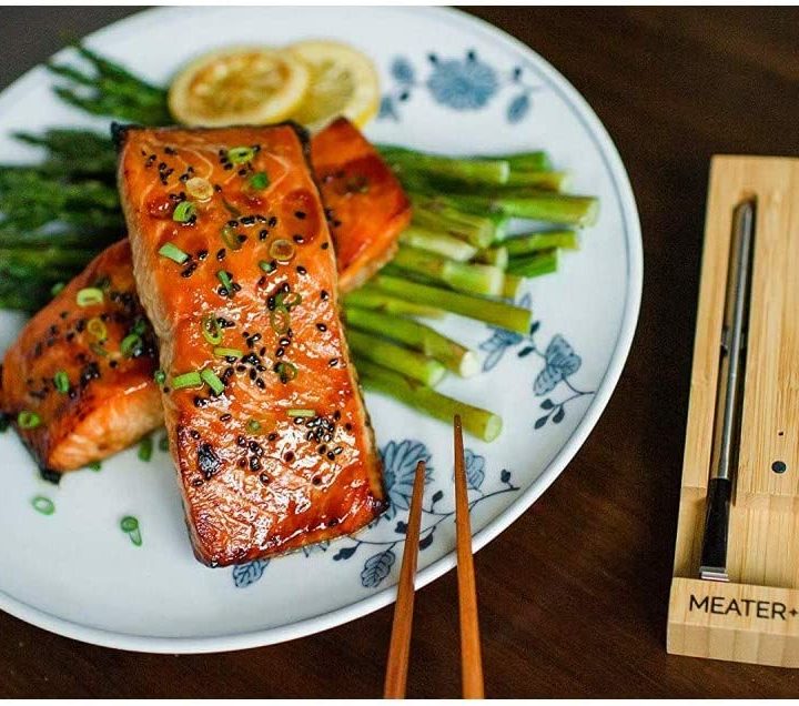 The Meater thermometer in its wooden case next to a plate of cooked salmon.